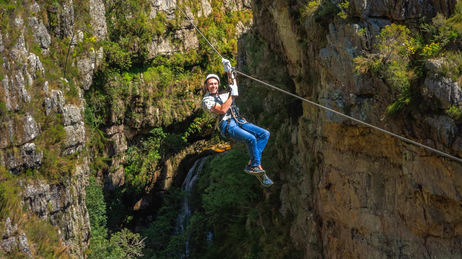 A guest smiling mid-slide on a zipline high above a gorge near Cape Town